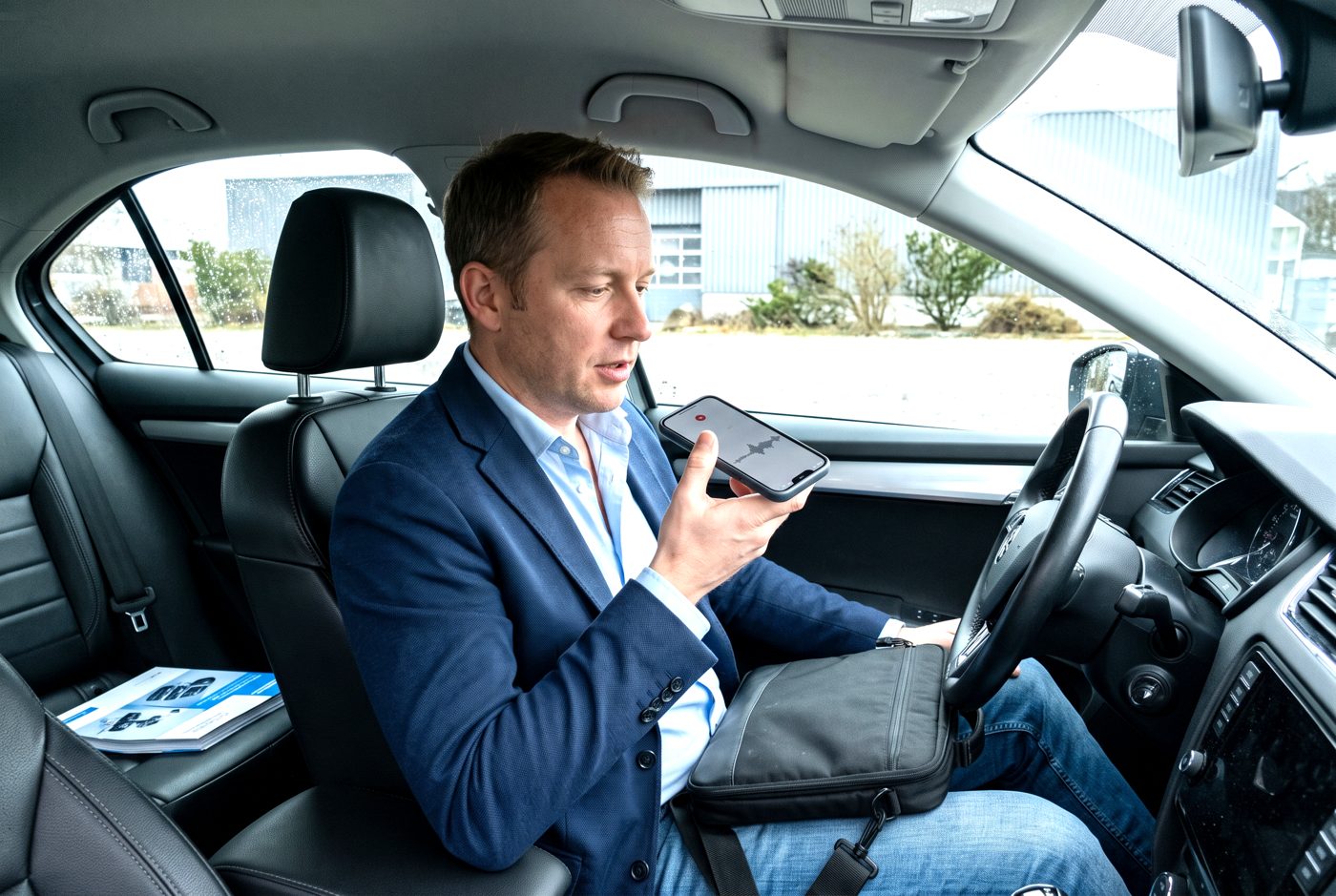 Verkäufer diktiert nach dem Kundenbesuch im Auto seinen Besuchsbericht ins Smartphone